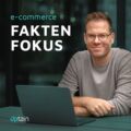 Julian Craemer, Moderator des E-Commerce Podcasts 'Faktenfokus' von uptain sitzt entspannt mit einem Laptop am Tisch, lächelnd in die Kamera