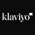 Klaviyo Logo in weißer Schrift auf schwarzem quadratischem Hintergrund, mit einem kleinen gefüllten Wimpel rechts oben am Wortende.